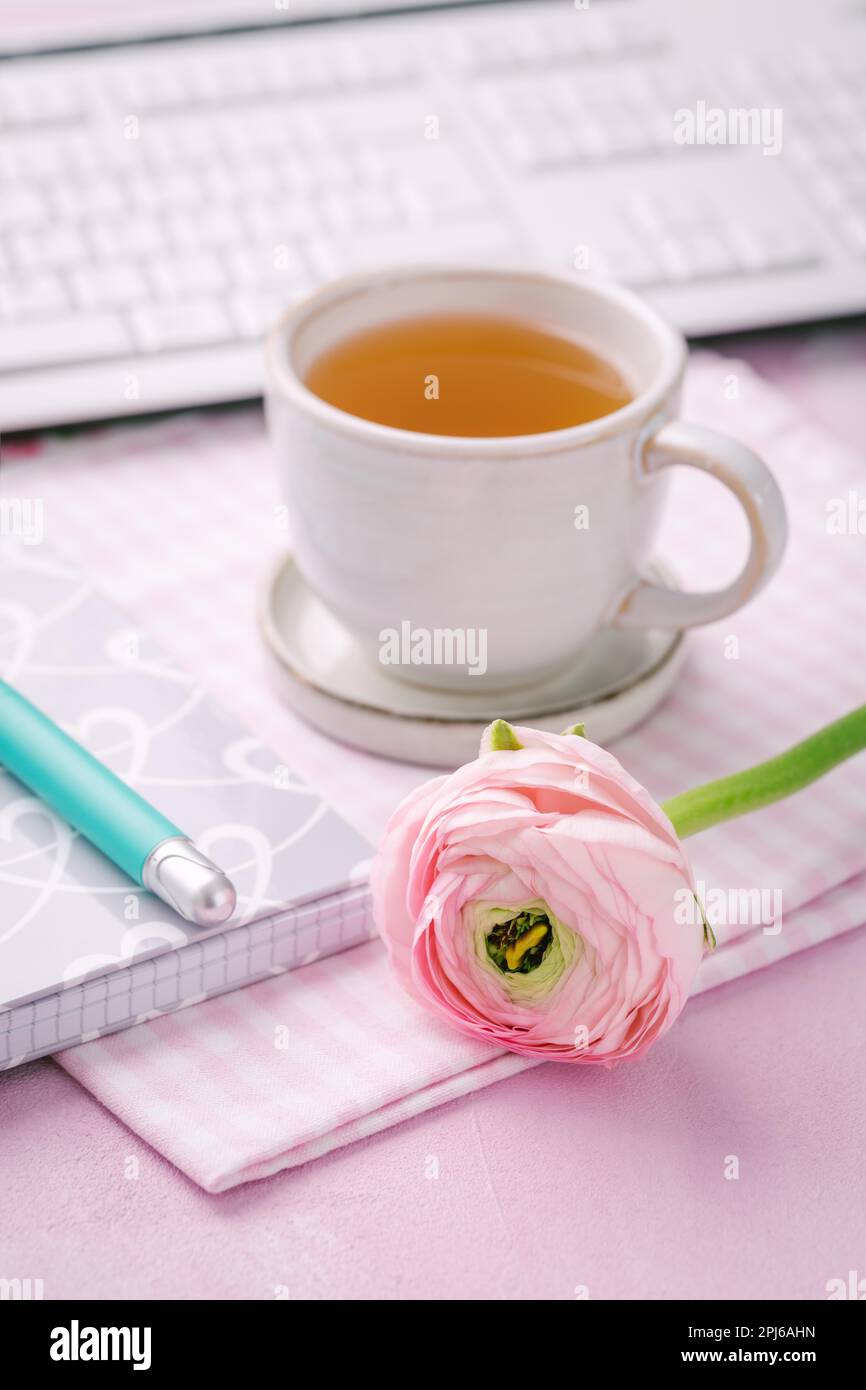 Scrivania da ufficio con tazza di tè, fiori, tastiere e articoli per la scrittura Foto Stock