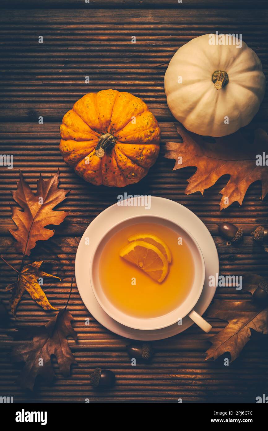 Tè caldo al limone con fogliame autunnale e zucche su sfondo di legno Foto Stock