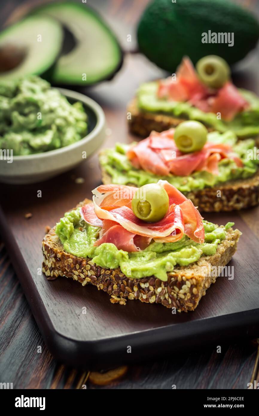 Guacamole tuffarsi o spalmare con sandwich e prosciutto aperti su tavolo da cucina in legno Foto Stock