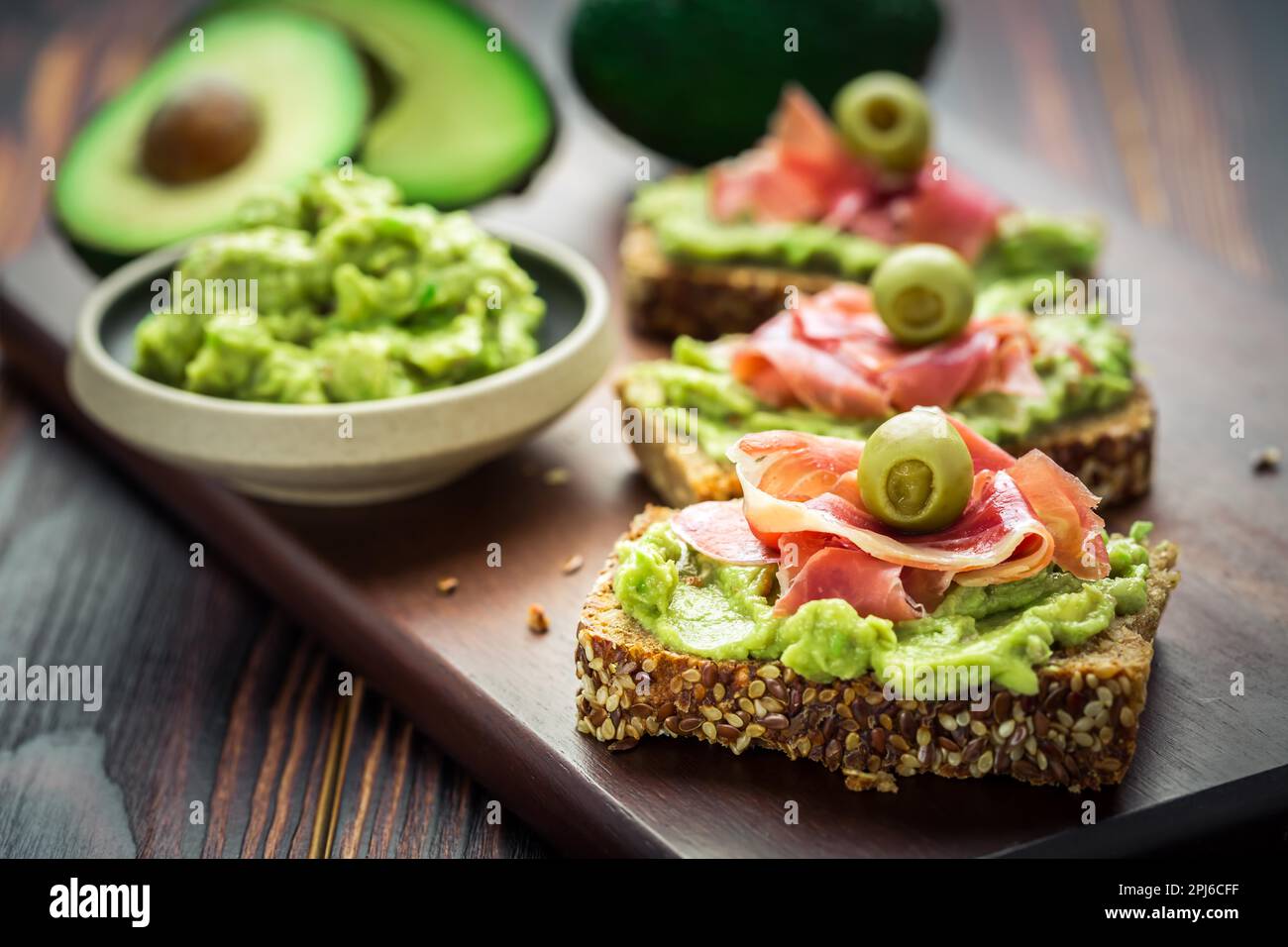 Guacamole tuffarsi o spalmare con sandwich e prosciutto aperti su tavolo da cucina in legno Foto Stock