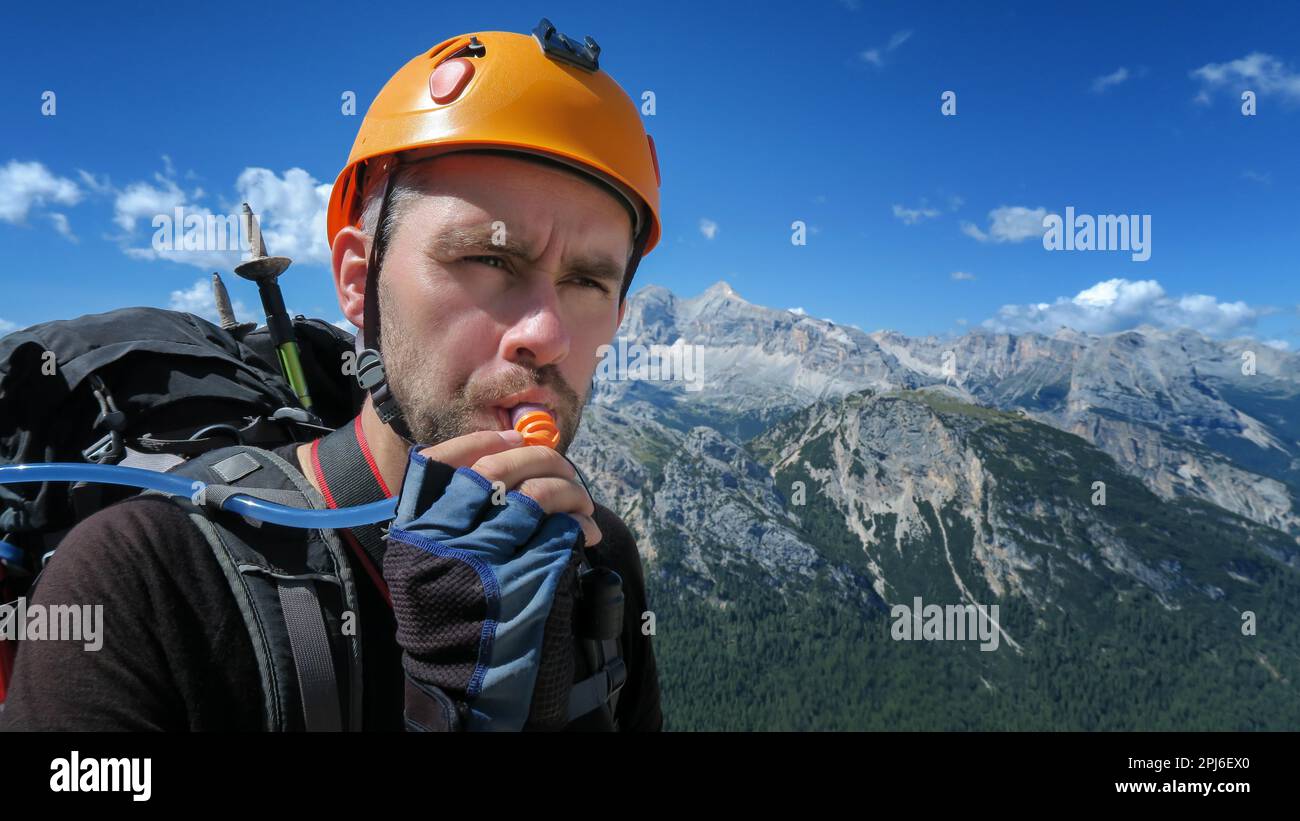 Un turista assetato beve acqua attraverso un tubo sullo sfondo di un panorama mozzafiato delle montagne delle Dolomiti. Dolomiti, Italia, Dolomiti Foto Stock