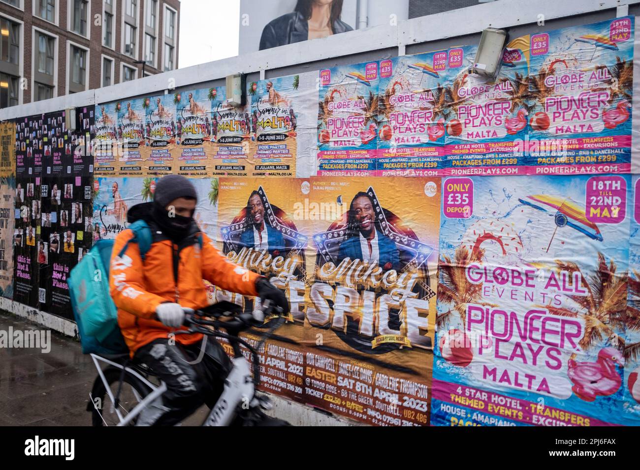 Street scene a Whitechapel, dove una guardia intorno a un cantiere edile è coperta da poster pubblicitari per varie serate di club il 8th marzo 2023 a Londra, Regno Unito. Foto Stock