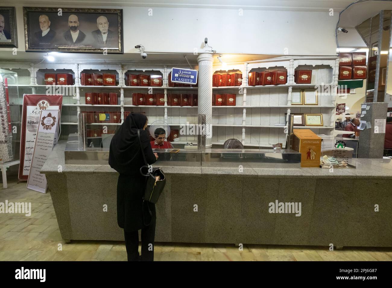 Donna musulmana di fronte a un contante in un negozio in Iran. Personale addetto alla cassa seduto dietro il bicchiere al bancone in un negozio. Donna che paga il conto Foto Stock