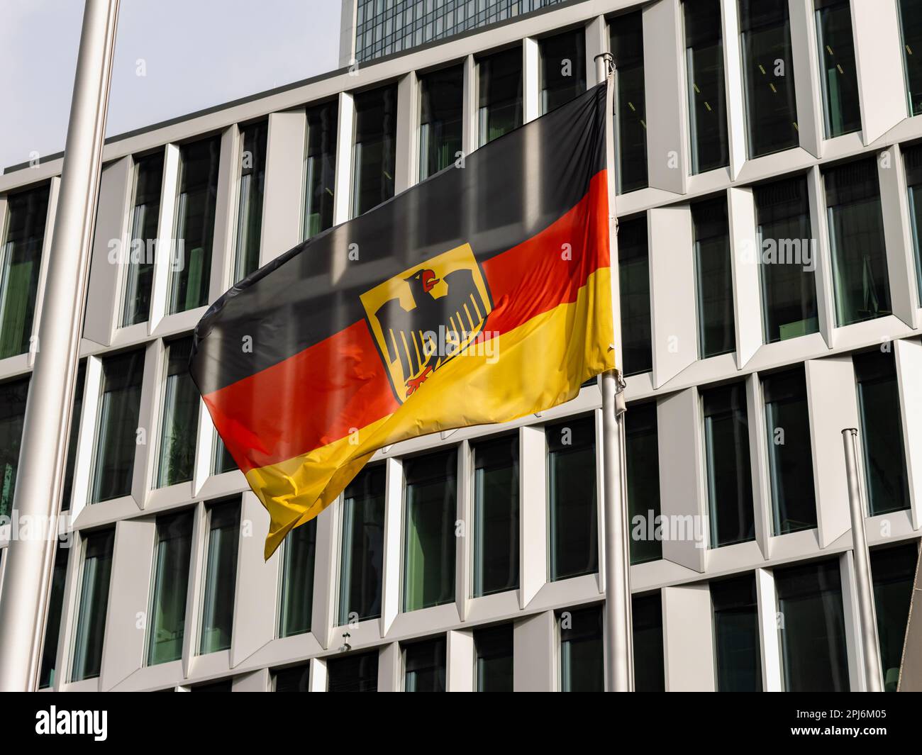 Bandiera tedesca di fronte all'esterno di un edificio di uffici. Il tessuto sta ondeggiando nel vento. È il simbolo della Germania e della cultura tedesca. Foto Stock