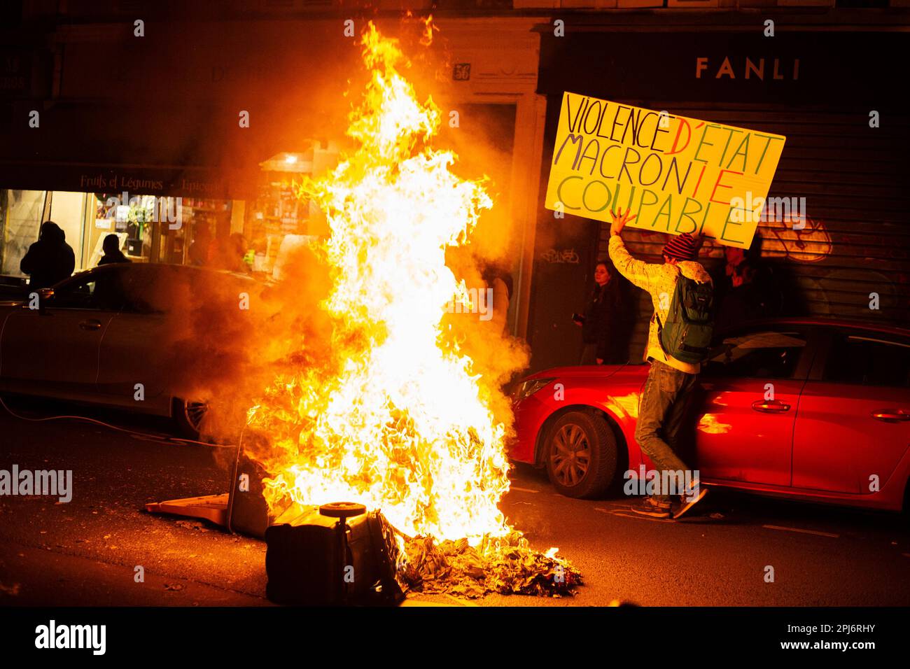 Parigi, Francia. 30th Mar, 2023. Un protettore tiene un cartello che dice 'violence d'etat Macron coupable' mentre passa vicino a un falò durante la manifestazione. Quasi 90 raduni sono stati organizzati nelle principali città del paese, di fronte alle prefetture e ai comuni contro la violenza della polizia. A Parigi migliaia di persone si sono riunite di fronte all'Hotel de Ville per chiedere le dimissioni del Ministro degli interni, Gerald Darmanin. Dopo la protesta si sono svolte manifestazioni selvagge in varie parti della città. Credit: SOPA Images Limited/Alamy Live News Foto Stock