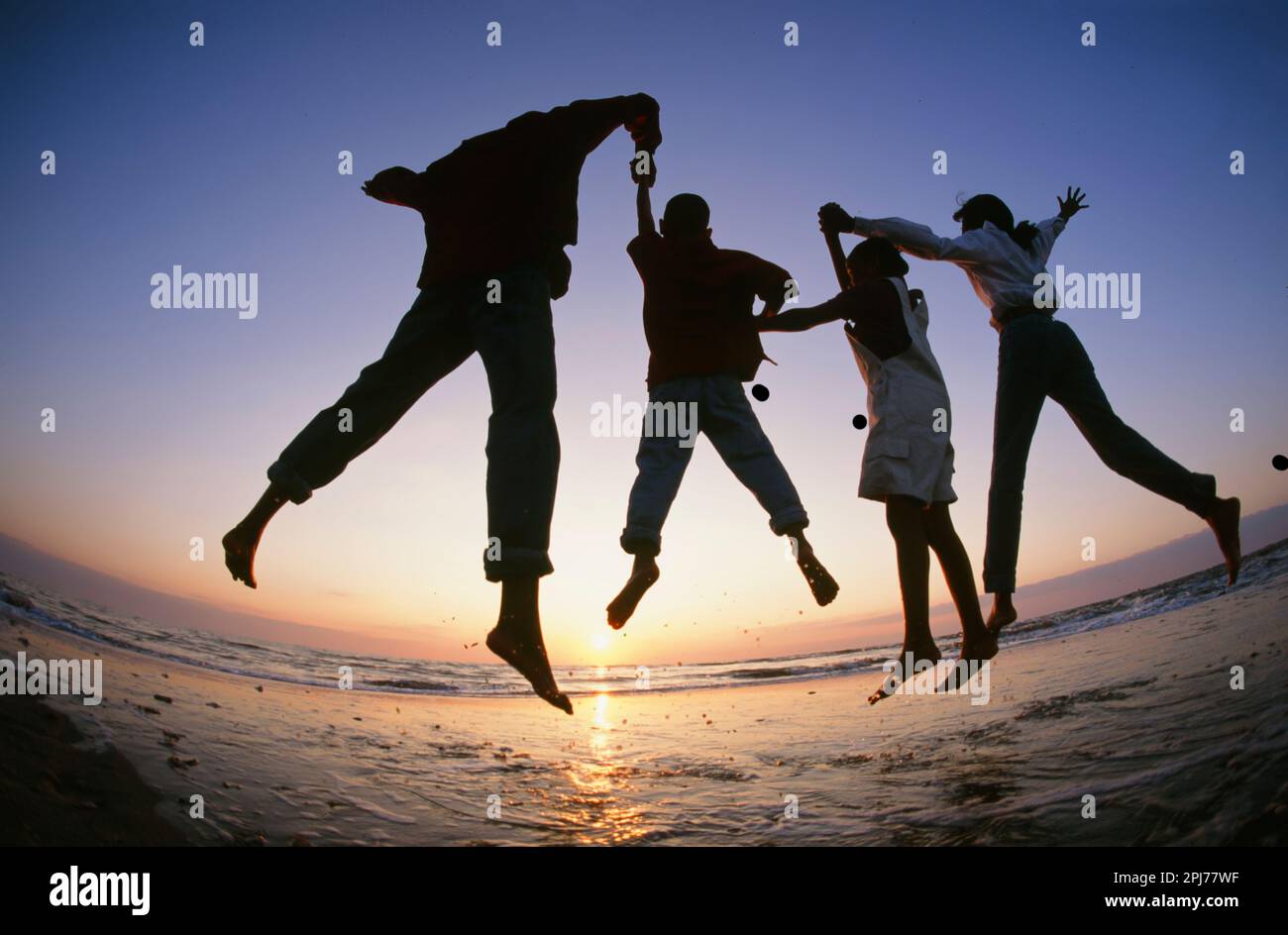 Una famiglia che salta per gioia mentre guardano l'alba sull'Oceano Atlantico Foto Stock