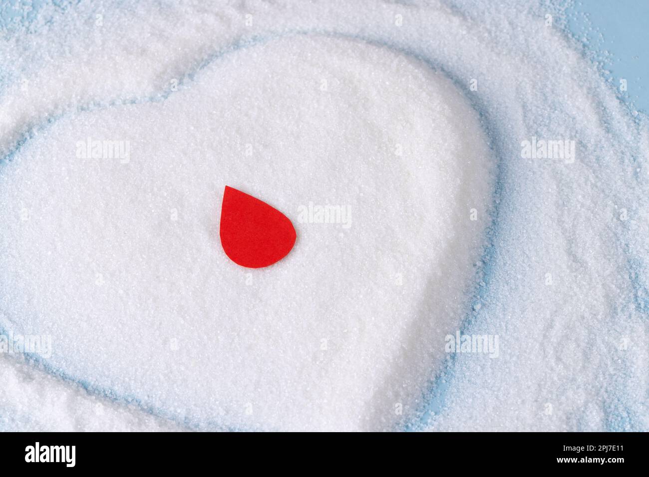 Goccia di sangue sullo zucchero a forma di cuore su sfondo blu Foto Stock