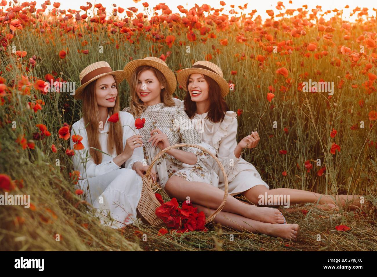 Ragazze divertenti in abiti e cappelli in un campo papavero al tramonto. Foto Stock
