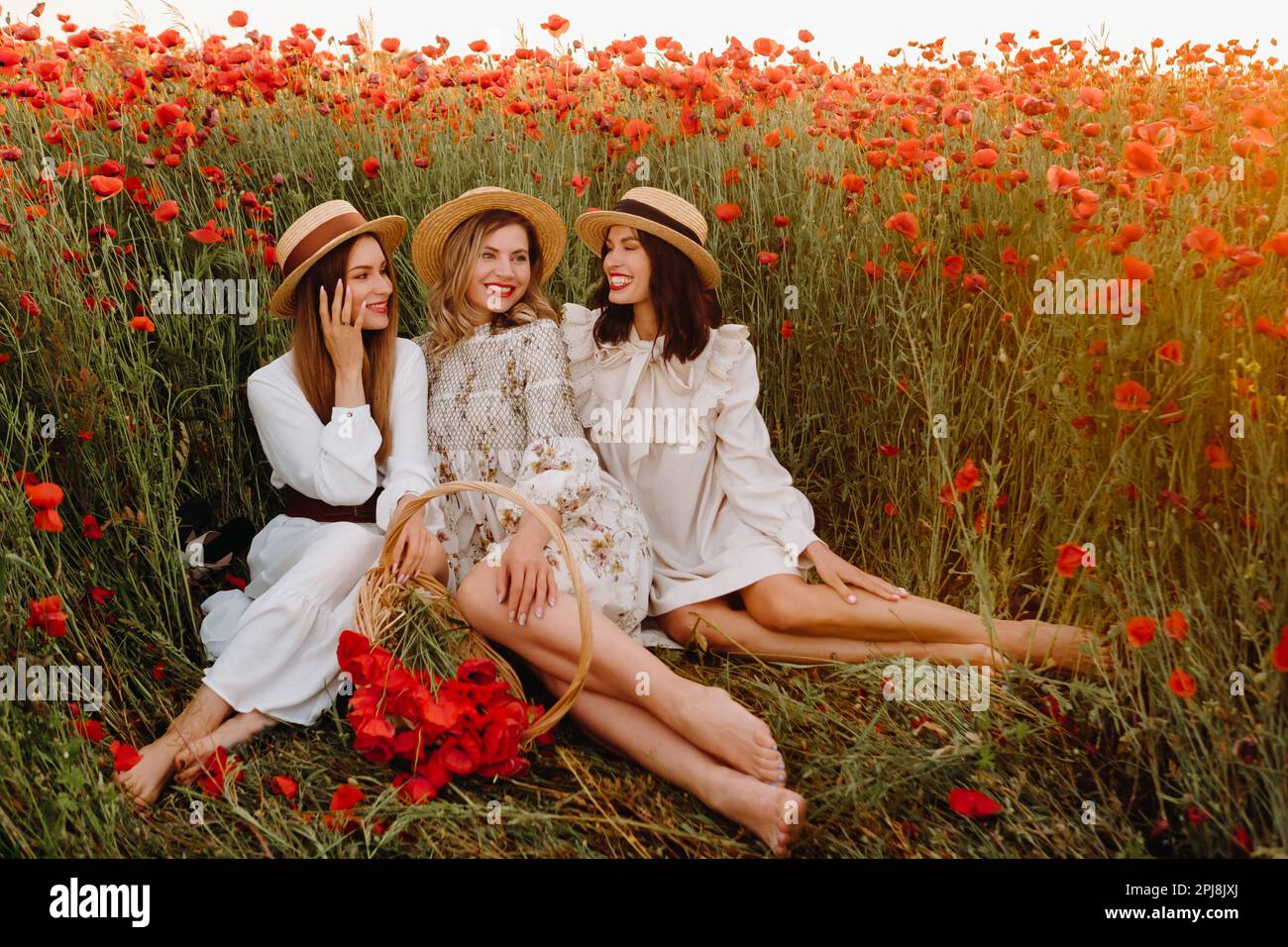 Ragazze divertenti in abiti e cappelli in un campo papavero al tramonto. Foto Stock