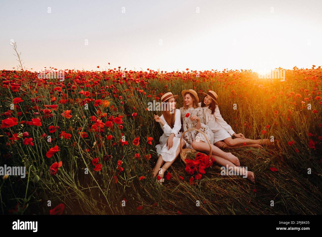 Ragazze divertenti in abiti e cappelli in un campo papavero al tramonto. Foto Stock