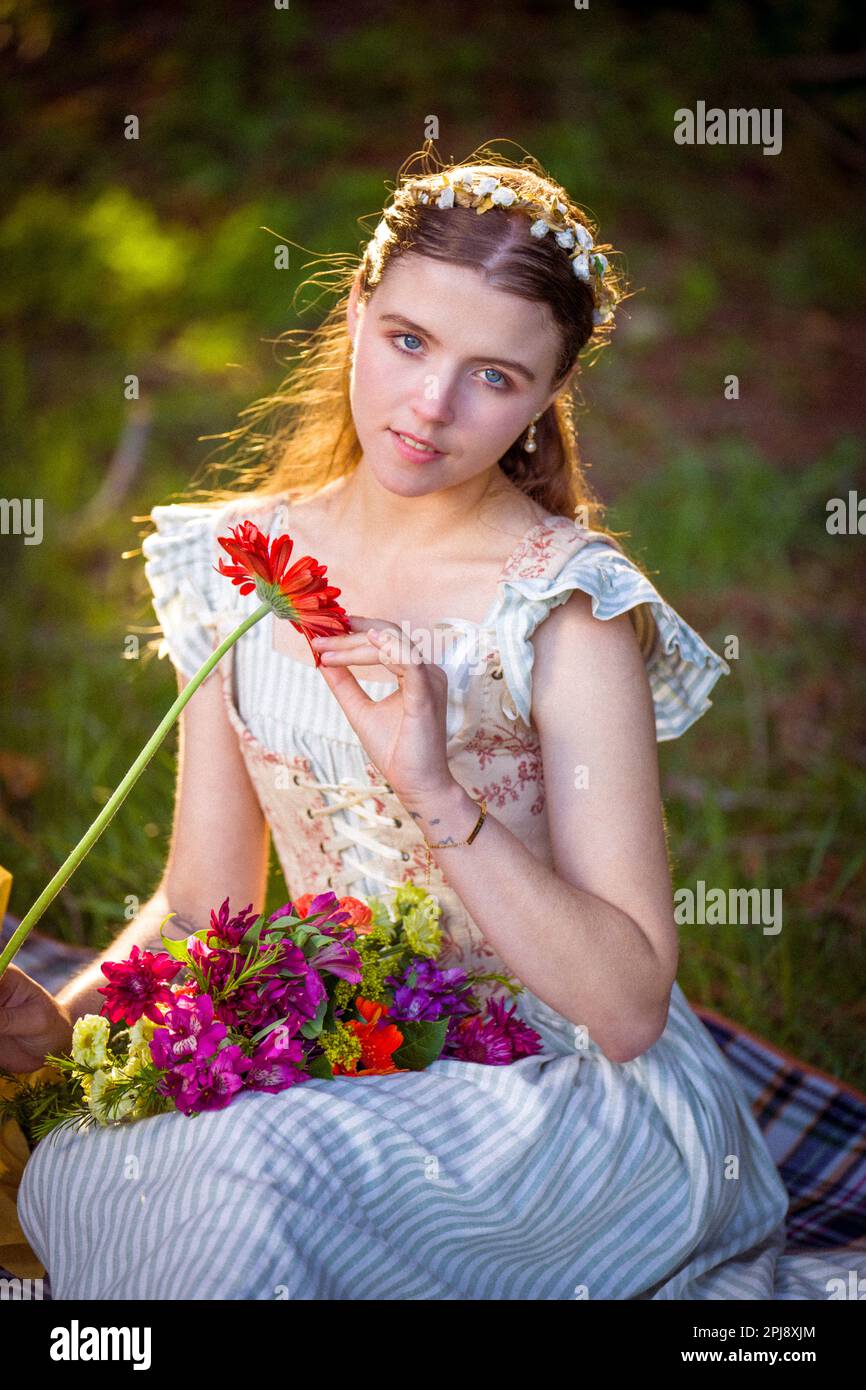 Giovane donna che indossa corpetto e abito allacciato seduto su una coperta e tenendo un bouquet di fiori | Fiore Hairband | colori caldi Foto Stock