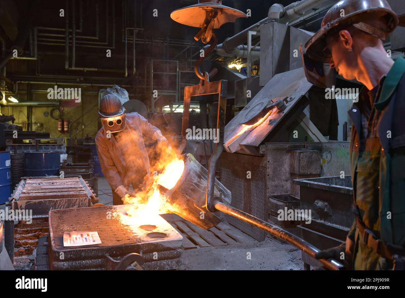 I lavoratori in un getto di fonderia di un pezzo di metallo - Sicurezza sul lavoro e il lavoro di squadra Foto Stock