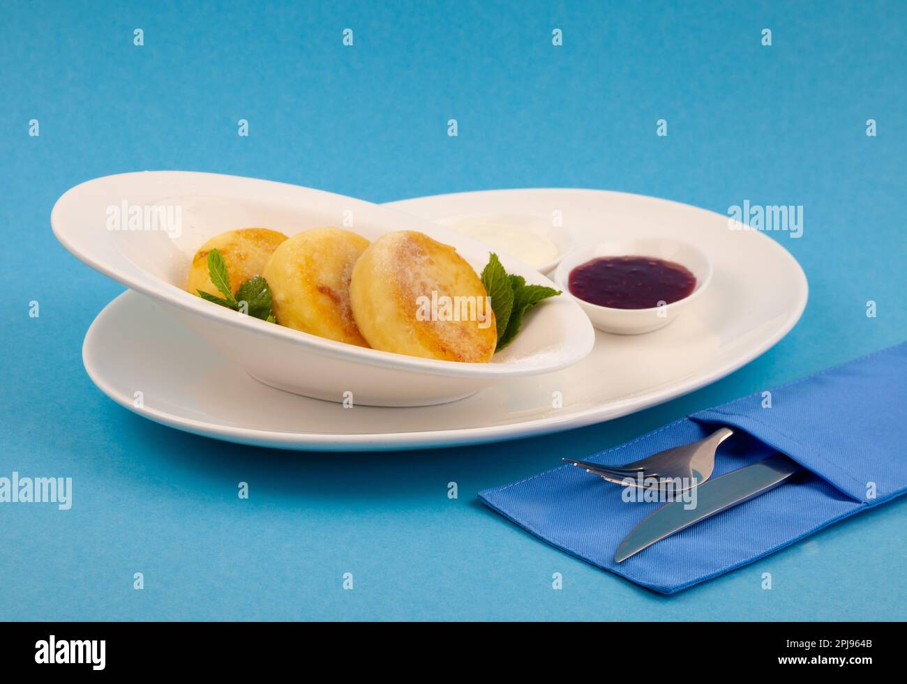 Frittelle di formaggio ricotta rotonda in un piatto bianco su sfondo blu. Cibo prima colazione. Cibo sano. Salsa di panna acida e menta. Primo piano vista dall'alto. Pasto dessert. Frittelle di ricotta al formaggio ricotta. Foto Stock