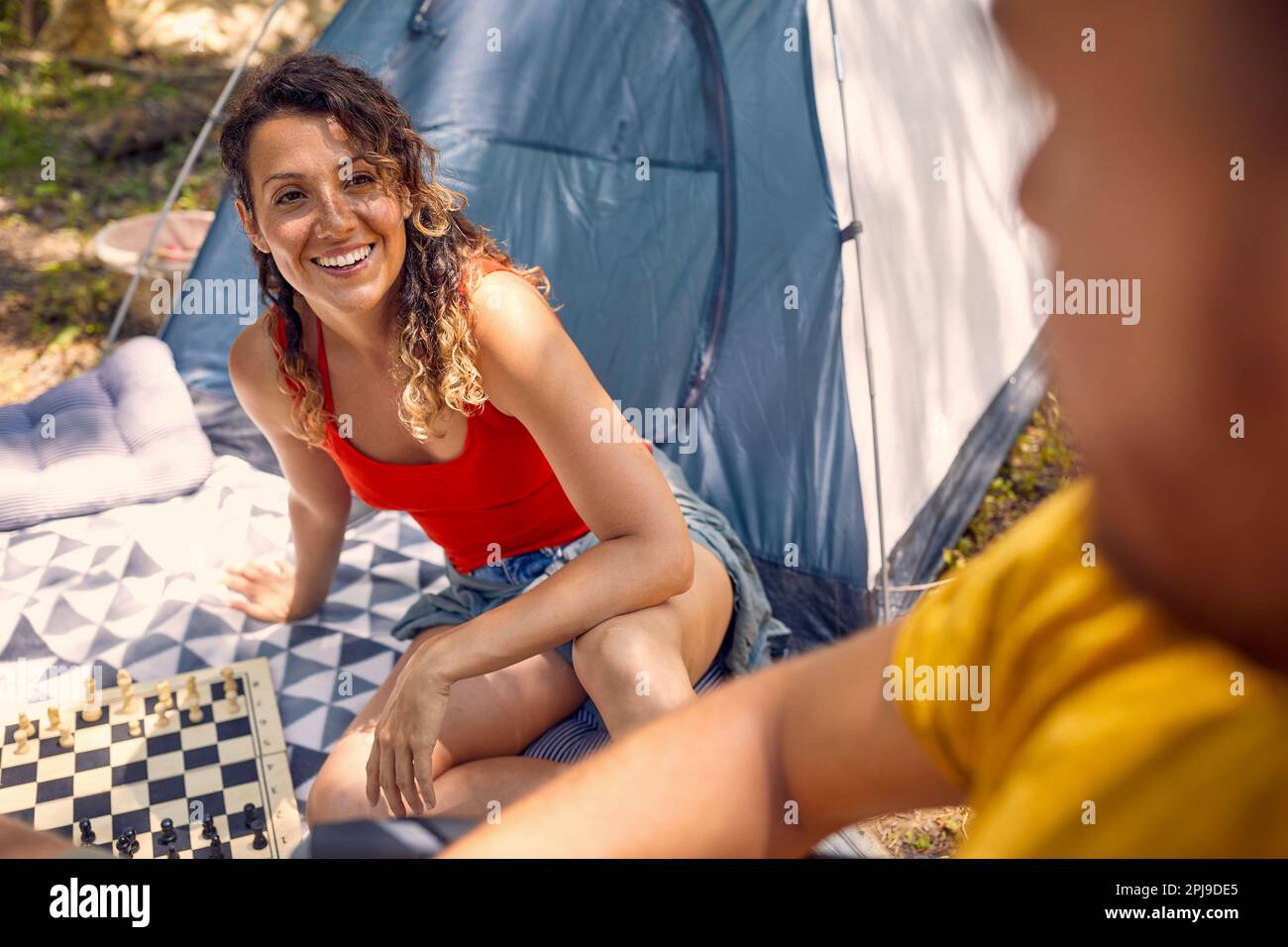 Amici campeggio nella natura. Giovane uomo e donna che giocano a scacchi a terra, godendosi un picnic nella foresta. Concetto di convivenza, vacanza, stile di vita. Foto Stock