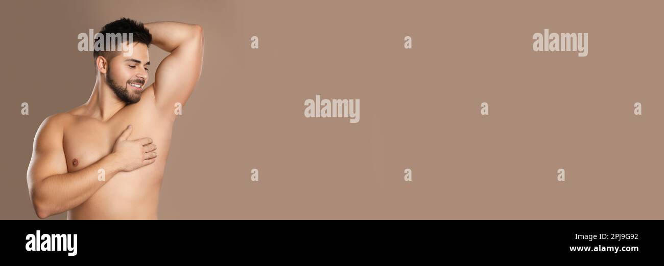 Giovane uomo che mostra l'ascella dopo l'applicazione del deodorante su sfondo marrone, spazio per il testo. Design del banner Foto Stock