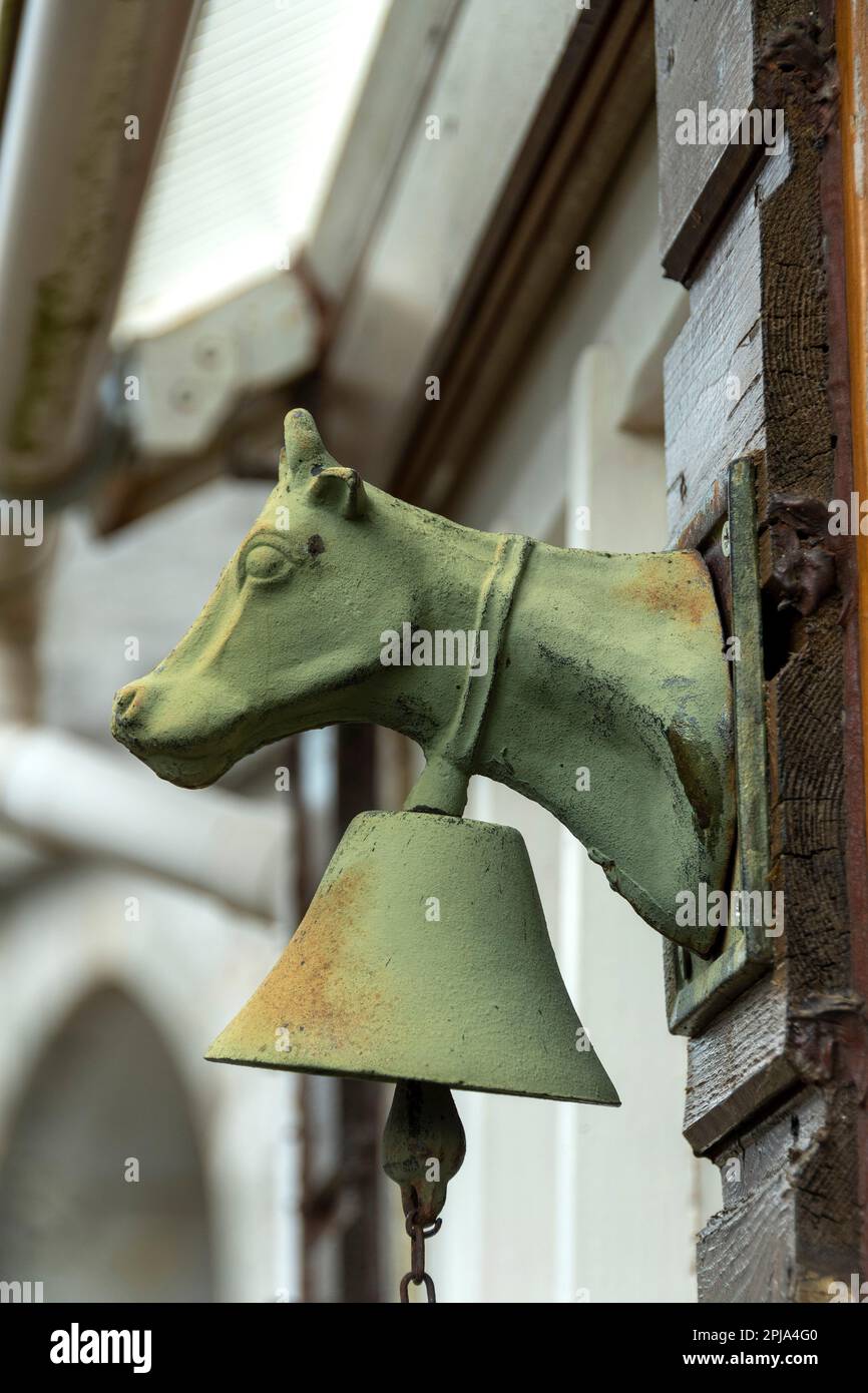 Campana rustica a forma di mucca montata su un muro di legno in una fattoria rurale durante il giorno, Auvergne, Francia Foto Stock
