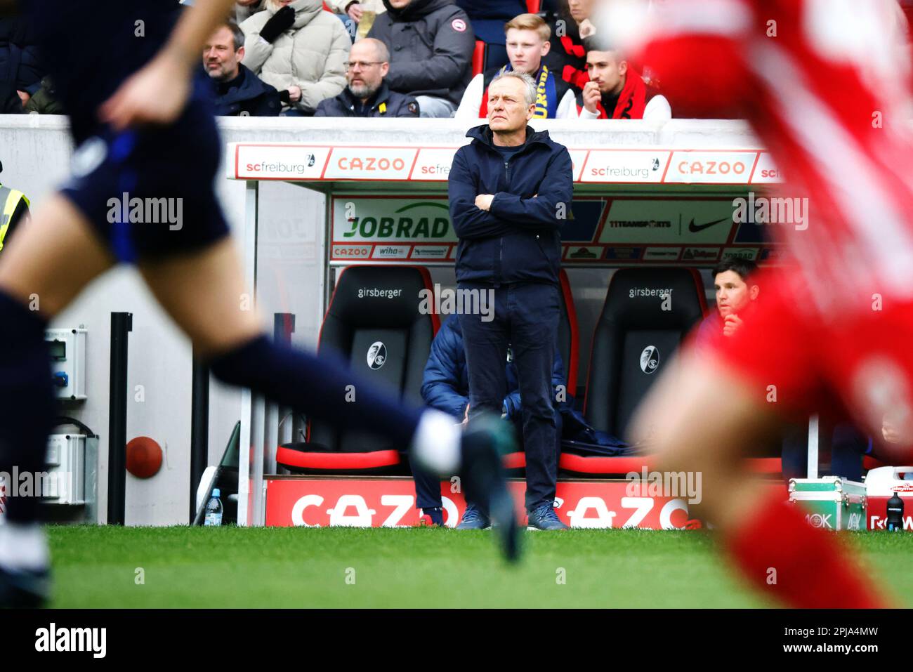 01 aprile 2023, Baden-Württemberg, Freiburg im Breisgau: Calcio: Bundesliga, SC Freiburg - Hertha BSC, giorno 26, Europa-Park Stadion: L'allenatore capo di Friburgo Christian Streich si trova a margine, mentre i giocatori di Hertha BSC Berlin e SC Freiburg possono essere visti in primo piano. Foto: Philipp von Ditfurth/dpa - NOTA IMPORTANTE: In conformità ai requisiti della DFL Deutsche Fußball Liga e della DFB Deutscher Fußball-Bund, è vietato utilizzare o utilizzare fotografie scattate nello stadio e/o della partita sotto forma di sequenze di immagini e/o serie di foto simili a video. Foto Stock