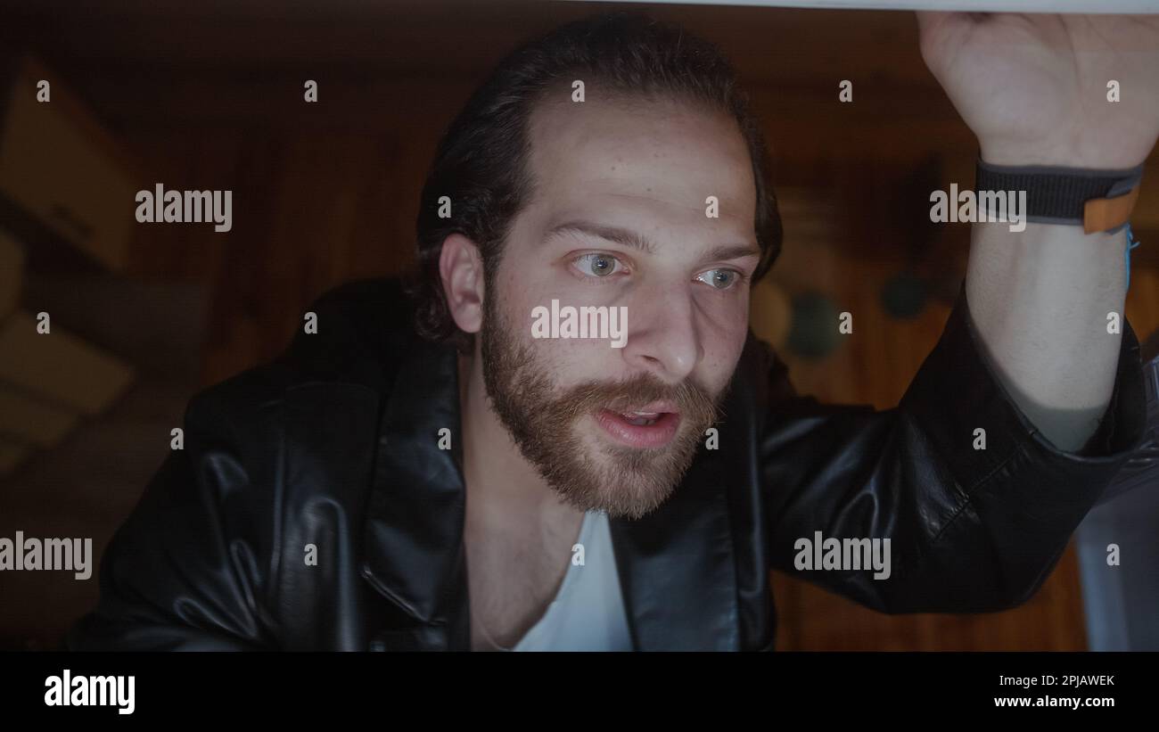 Bell'uomo con capelli lunghi e giacca nera apre la porta del frigorifero per afferrare uno spuntino Foto Stock