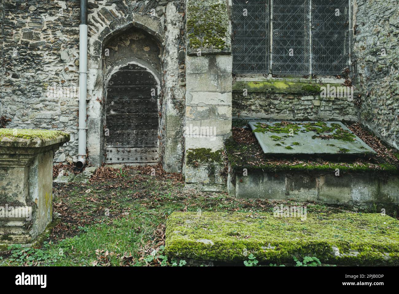 Vista dettagliata dell'ingresso di una chiesa medievale che mostra la porta della cripta. Il muschio umido è visibile sulle superfici a causa dell'ombra quasi costante. Foto Stock