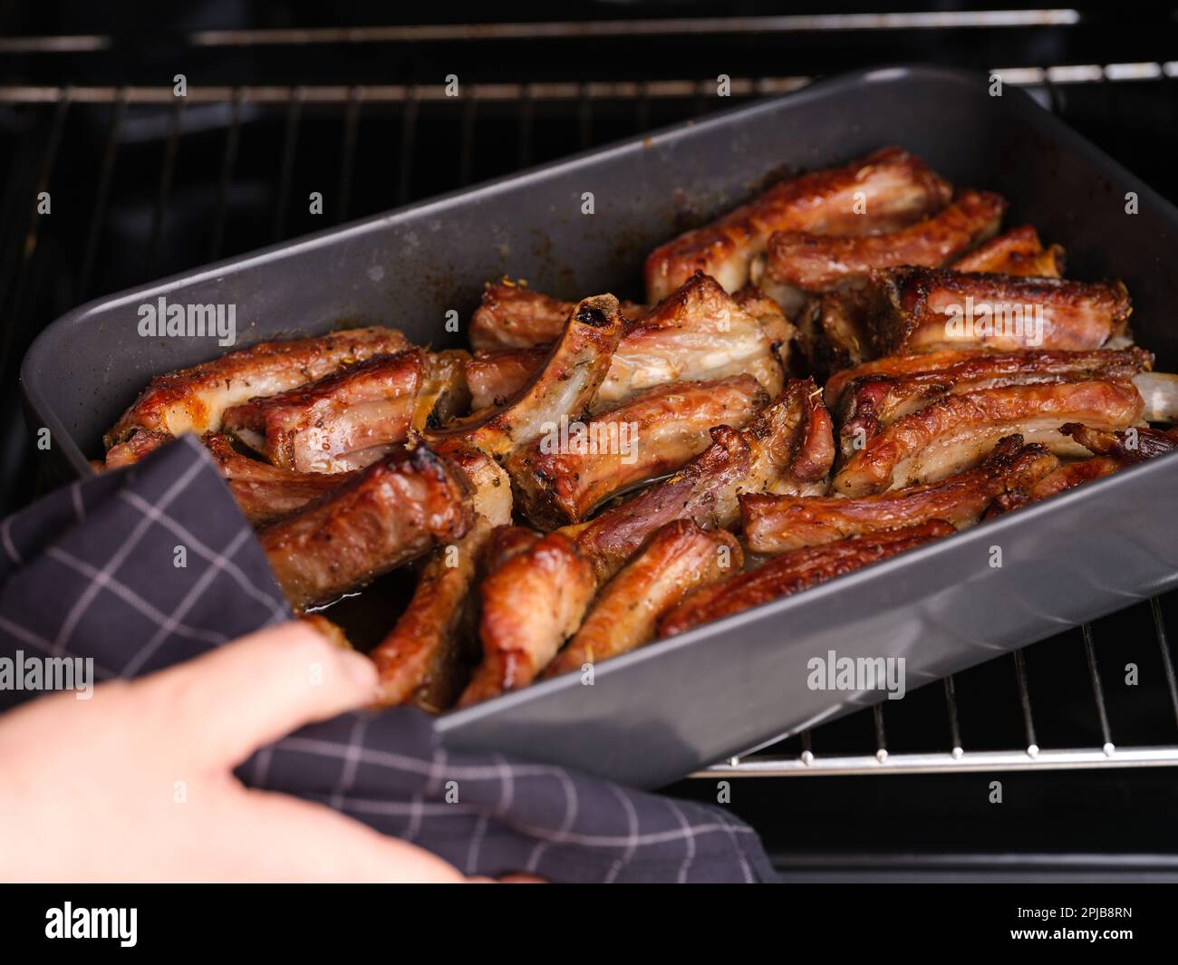 Donna che prende un vassoio da forno nero con costolette di maiale al forno. Foto Stock