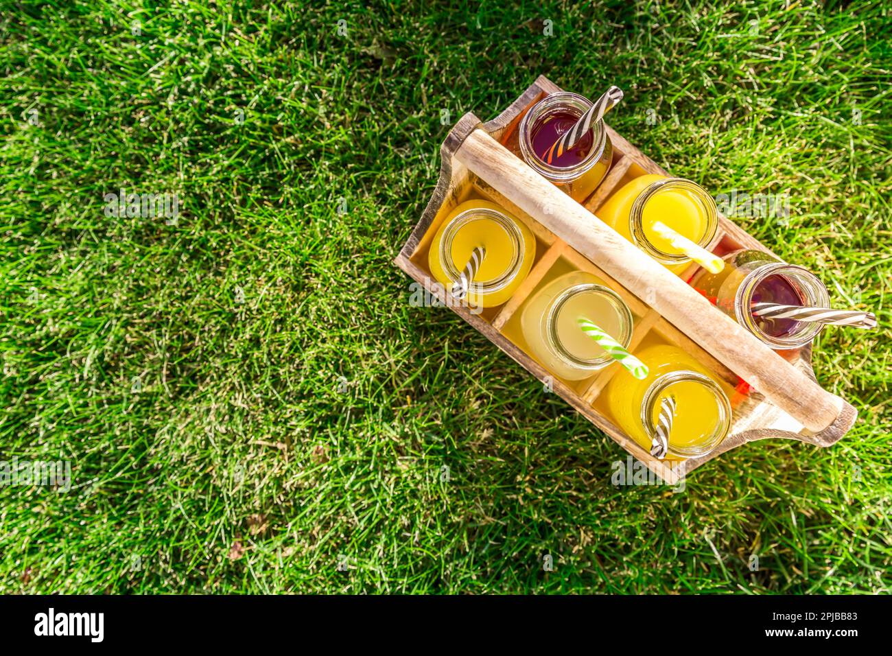 Assortimento di limonata e tè ghiacciato in bottiglie in rastrelliera di legno in erba Foto Stock