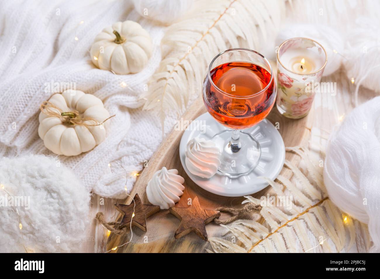 Accogliente still life per l'inverno e l'autunno con un bicchiere di vino rosa, biscotti di zucca, lana e maglione caldo Foto Stock