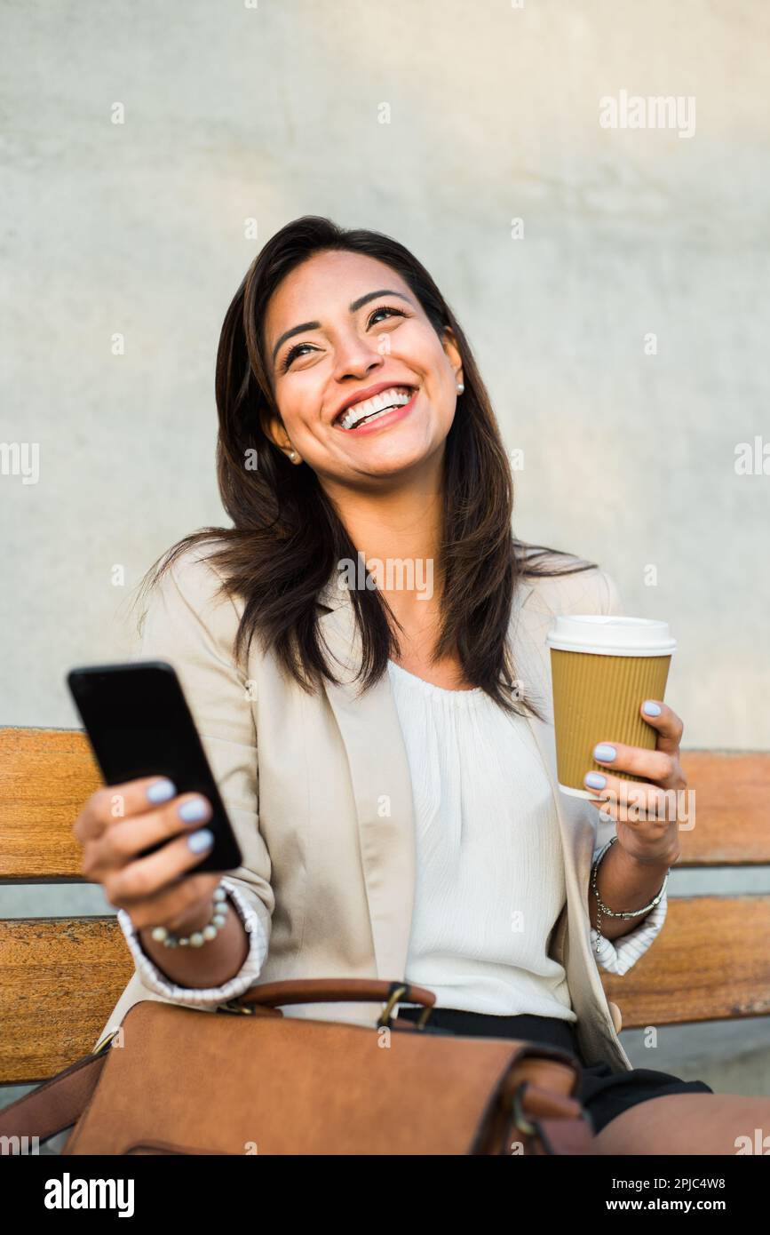 Immagine verticale di una donna d'affari di Latina felice e fiduciosa seduta a bere un drink e comunicando per telefono. Foto Stock