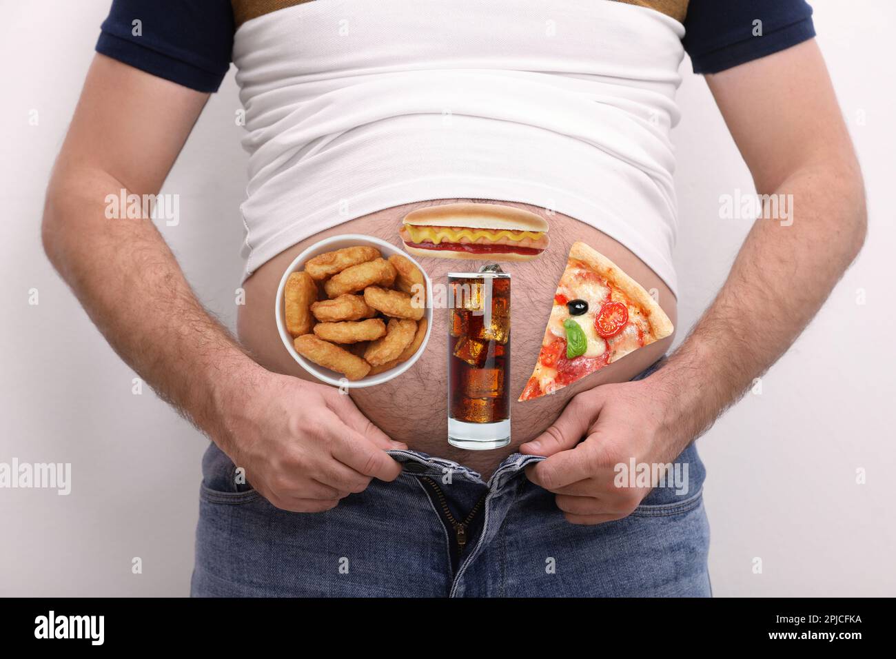 Uomo che indossa una t-shirt stretta e jeans con immagini di diversi cibi malsani sul ventre su sfondo bianco Foto Stock