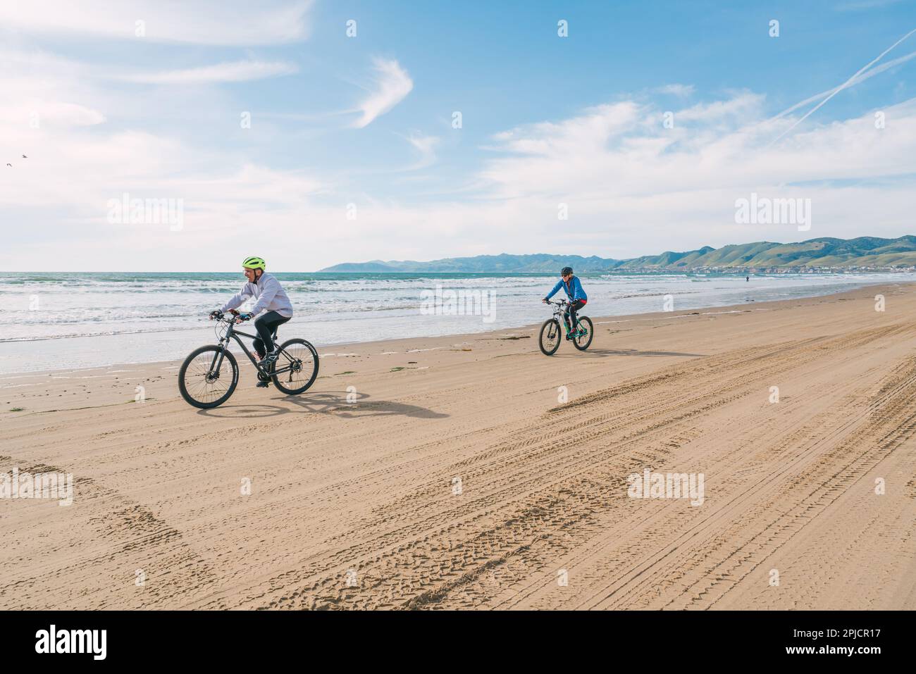 Oceano, California, USA - 27 marzo 2023. Coppia che indossa caschi da bicicletta a cavallo delle biciclette sulla spiaggia, California Central Coast Foto Stock