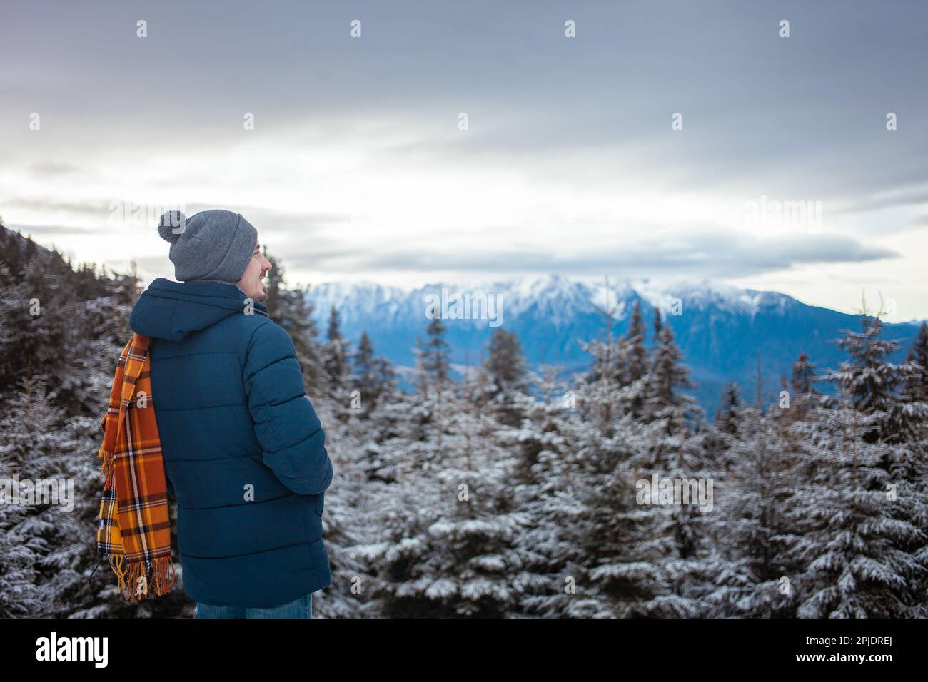 L'uomo ama guardare le montagne, il bellissimo panorama, la foresta e il cielo, l'inverno, la neve, viaggi, resort, escursioni, bellezza della natura. sciarpa arancione Foto Stock