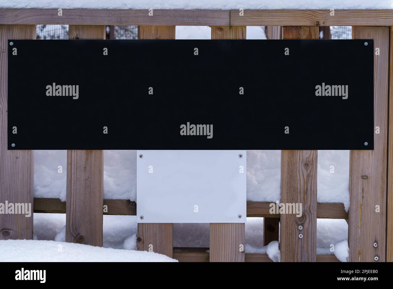 Ampio cartello nero con sotto un piccolo cartello bianco attaccato ad una recinzione in inverno. Foto Stock