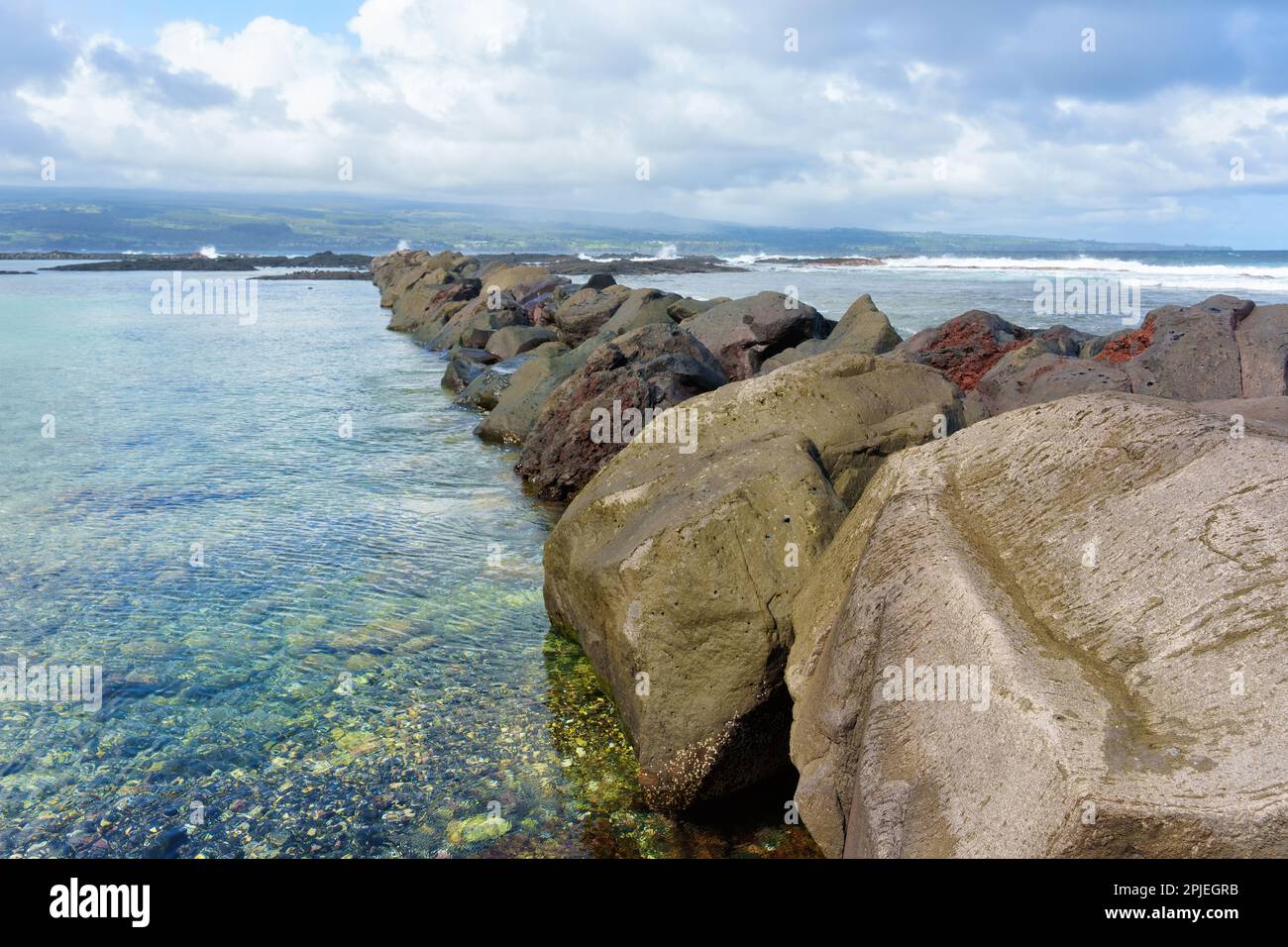 Pittoresca scena di una spiaggia hawaiana con grandi rocce che dividono la costa dall'oceano, incorniciata da un orizzonte oceano infinito e da nuvole ondulate ab Foto Stock
