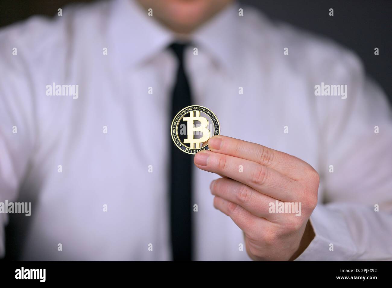 Un uomo d'affari in una camicia bianca e cravatta nera tiene una versione fisica di bitcoin nelle sue mani. Foto Stock