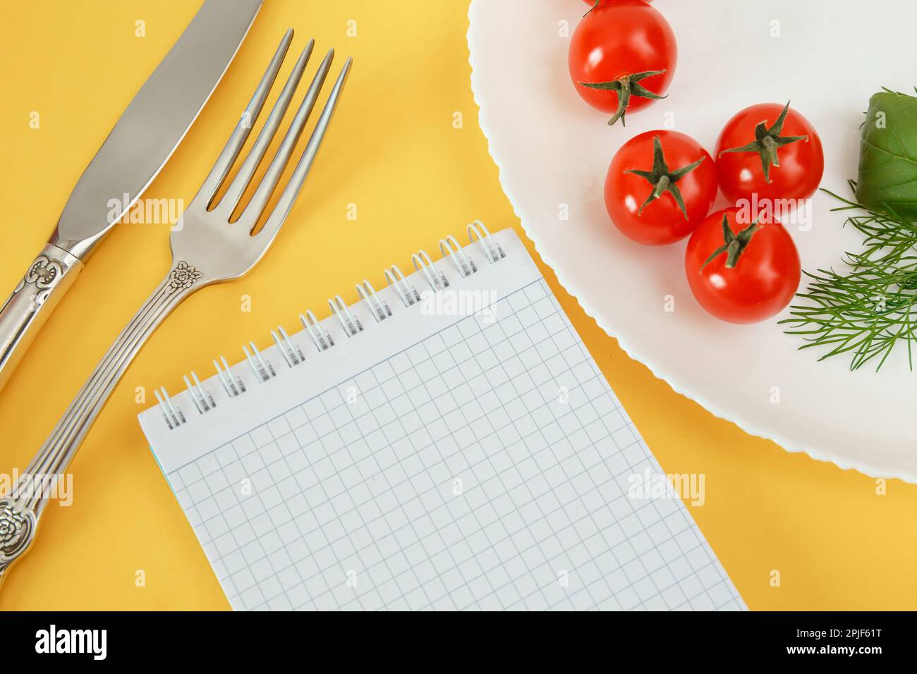 Pomodori ciliegini su un piatto con basilico e posate. Notebook per la registrazione e il conteggio delle calorie alimenti dietetici Foto Stock