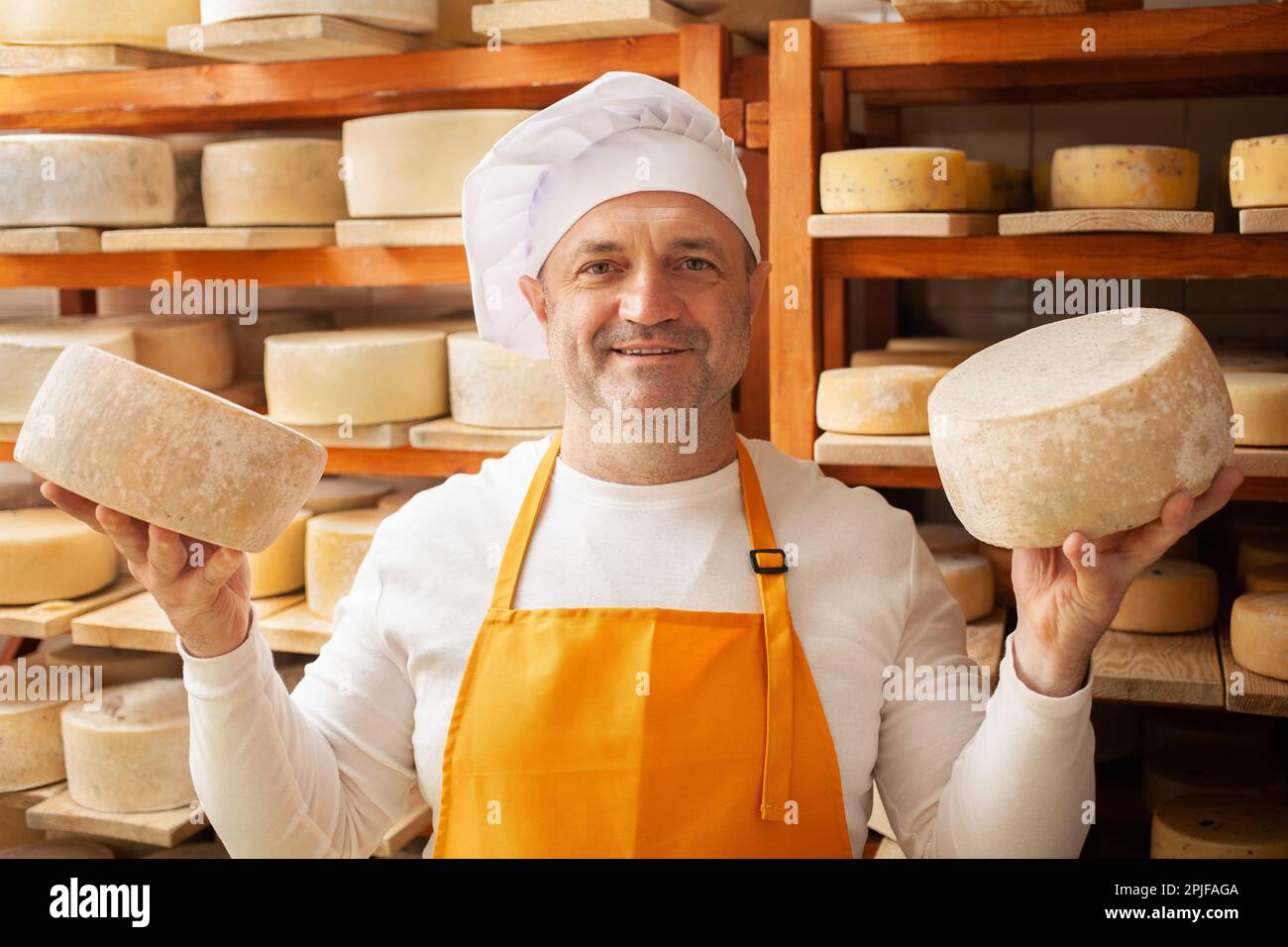 maschio, uomo produttore di formaggio uomo d'affari, imprenditore individuale, controlla il formaggio in cantina, seminterrato. la testa di formaggio matura su mensole di legno, processo di produ Foto Stock