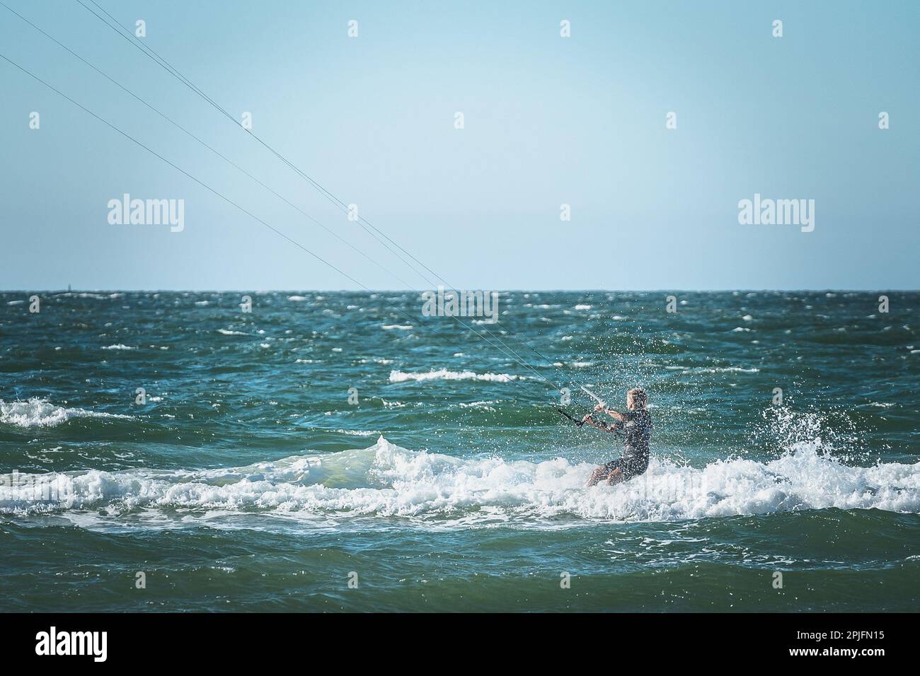 La gente gode di cavalcare kite surf board in tuta di protezione uv sole in giornata di sole al mare o mare spiaggia kitesurf campo spot. Sport acquatici adrenalina f Foto Stock