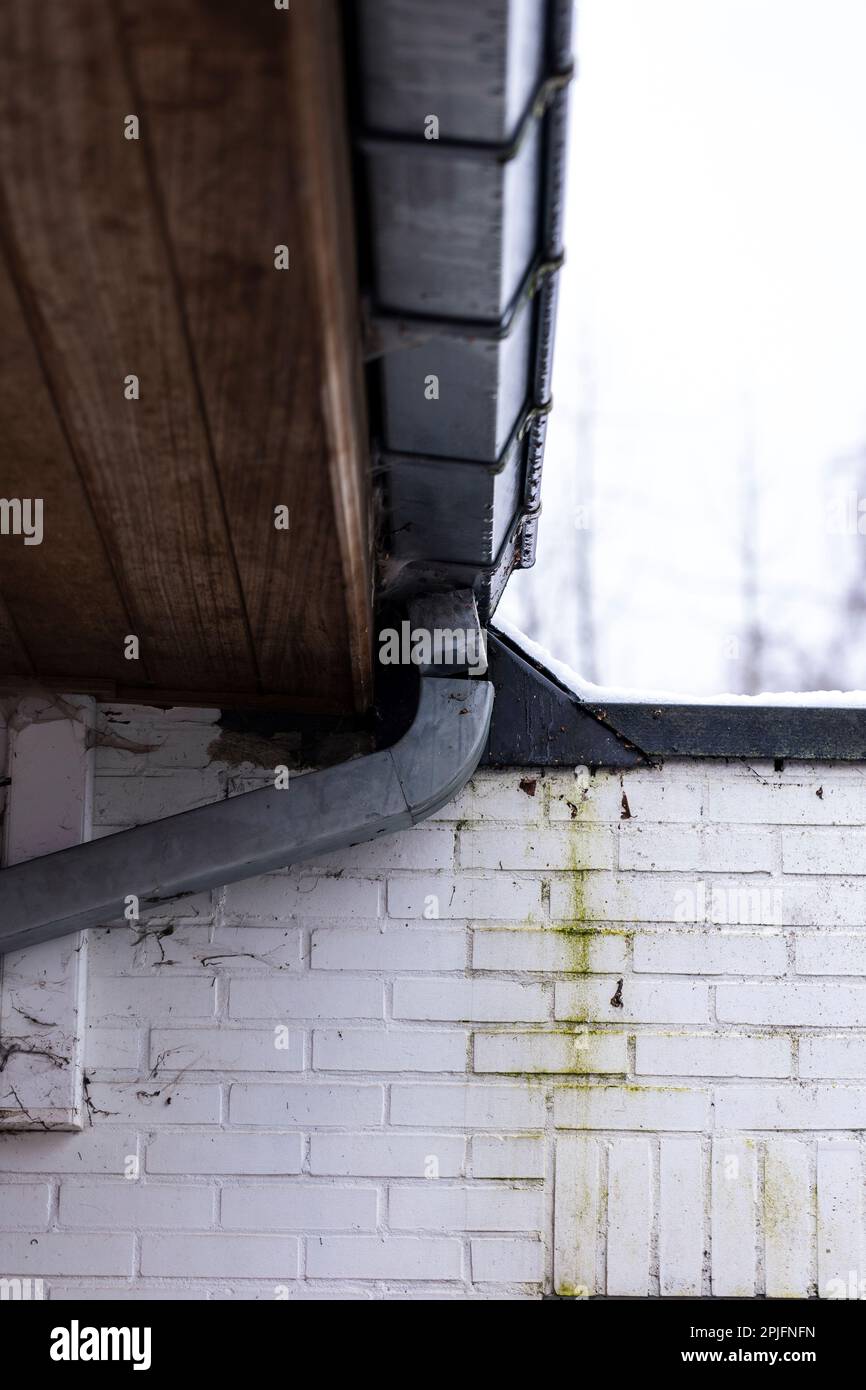 Un ritratto di un tubo di scarico in metallo rotto collegato alla grondaia di un tetto. Lo scarico necessita di riparazioni perché si è allentato poco prima dell'angolo. Foto Stock