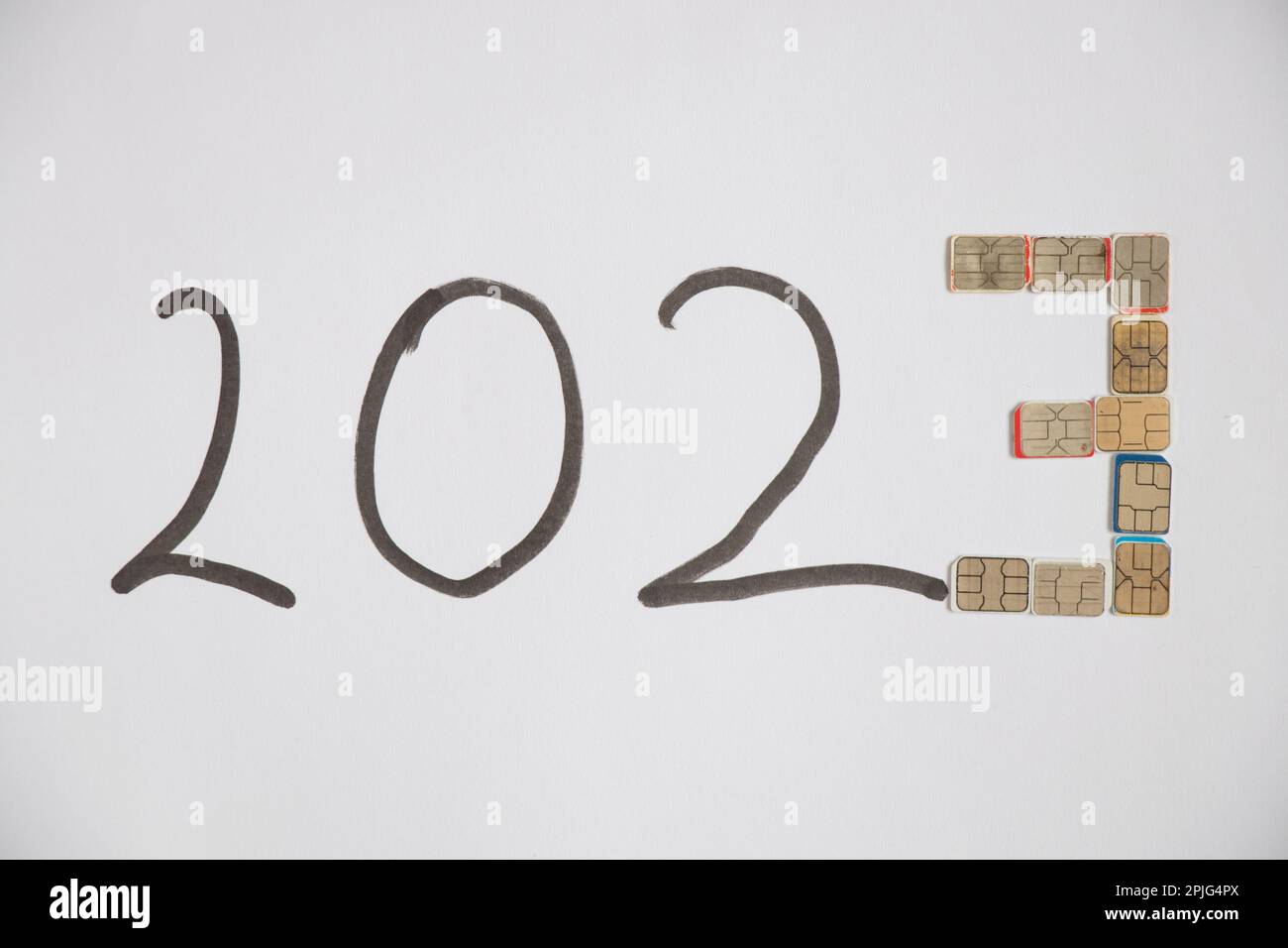 2023 è scritto con un marcatore nero e il numero tre è disposto dalle schede micro sim su uno sfondo bianco, un sostenitore mobile nel nuovo anno 20 Foto Stock