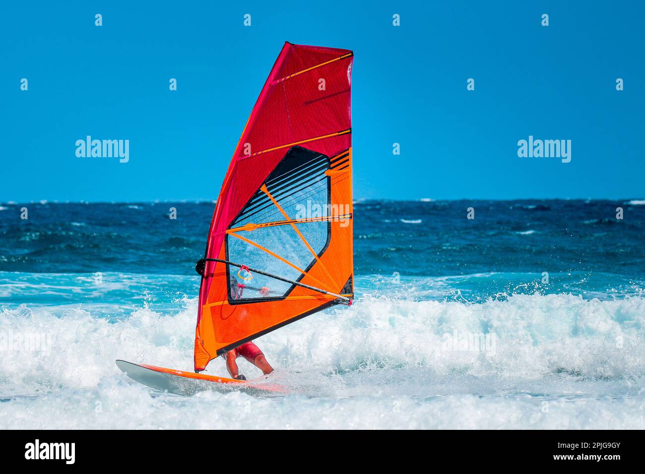 sport acquatici: windsurf con vela rossa e arancione che cavalcano le onde durante un pomeriggio estivo soleggiato. Foto Stock