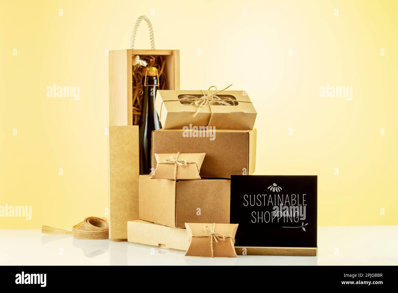 Eco friendly shopping e servizio di consegna. Scatole regalo in cartone, scatola in legno con bottiglia di champagne, lavagna con testo Sustainable Shopping Foto Stock