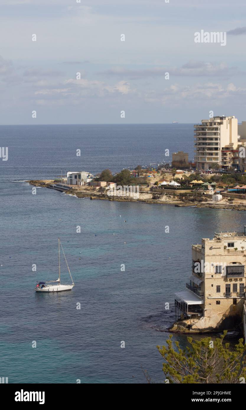 Uno yacht a vela ancorato a Balluta Bay a St Julian's, Malta. I mari d'alto mare si schiantano su affioramenti rocciosi. Zona popolare per sub aqua e snorkeling. Foto Stock