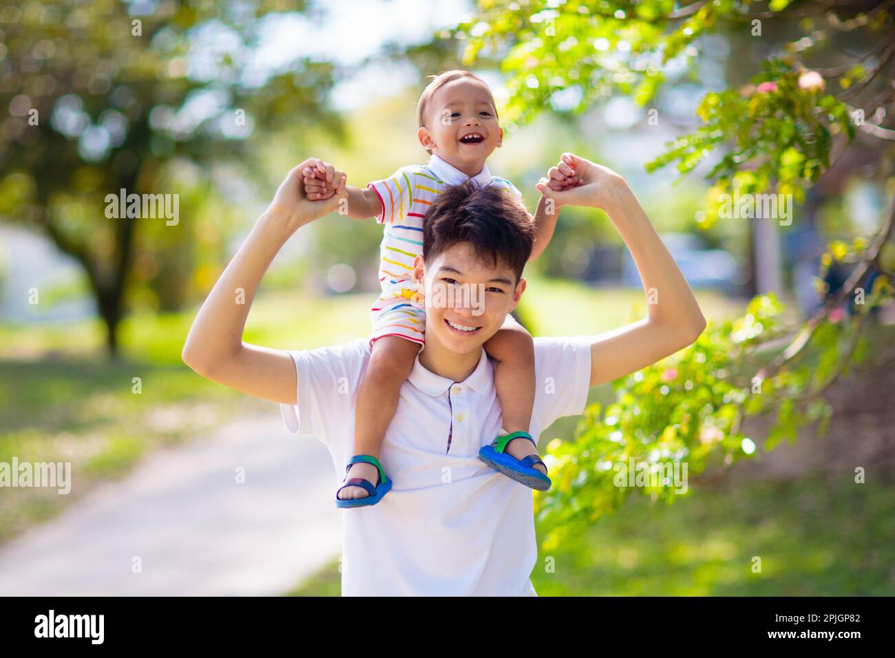 Ragazzo asiatico adolescente che gioca con suo fratello bambino. I fratelli si divertono nel parco estivo. Fratelli con grande differenza di età. Bambino della scuola che abbraccia il bambino piccolo Foto Stock