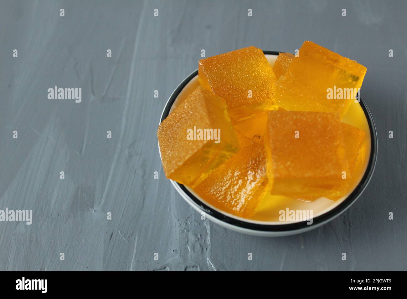 arancio marmellata arancione in un piatto piatto da ciotola su sfondo grigio con una miscela di testo. dessert sano su agar. Cubetti di arancia pezzi di marmellata. Foto Stock