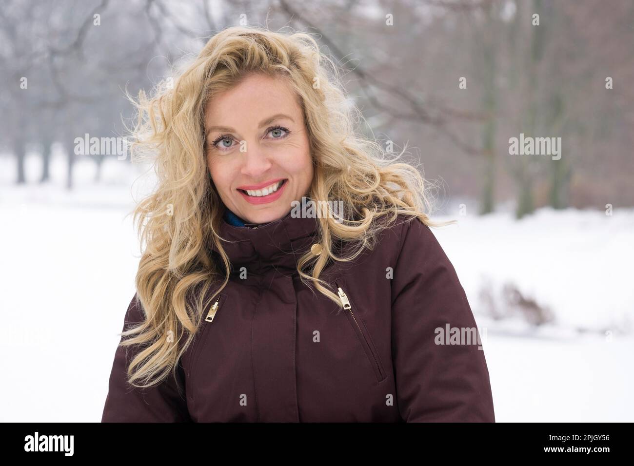donna bionda che si gode una passeggiata invernale attraverso il parco coperto di neve Foto Stock