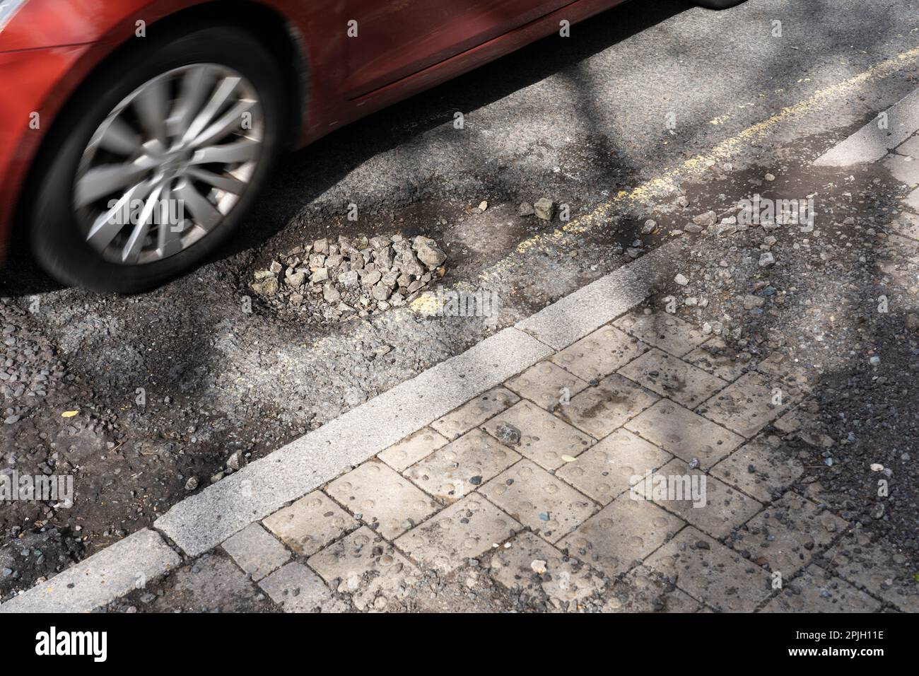Auto che passa per una grande buche su Winchester Road, Basingstoke, Regno Unito. La carenza di finanziamenti per la manutenzione locale delle strade è più elevata per anni. Marzo 2023 Foto Stock