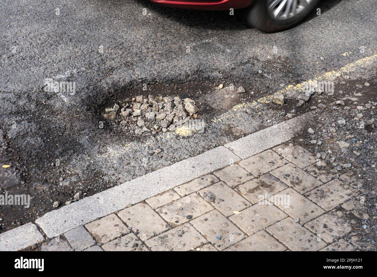 Auto che passa per una grande buche su Winchester Road, Basingstoke, Regno Unito. La carenza di finanziamenti per la manutenzione locale delle strade è più elevata per anni. Marzo 2023 Foto Stock