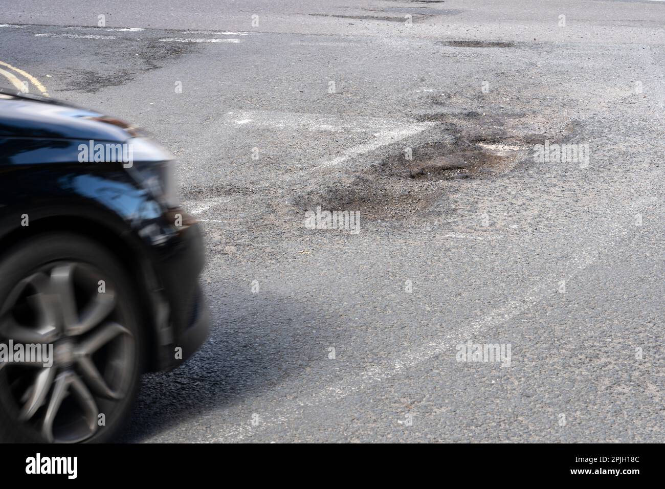 L'auto si avvicina a grandi buche su Winchester Road, Basingstoke, Inghilterra. La carenza di finanziamenti per la manutenzione locale delle strade è più elevata per anni. Marzo 2023 Foto Stock