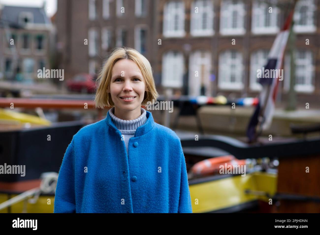 Donna adulta in cappotto sorridente mentre viaggia nei paesi bassi. Piacevoli escursioni e avventure. Una persona positiva. Foto Stock