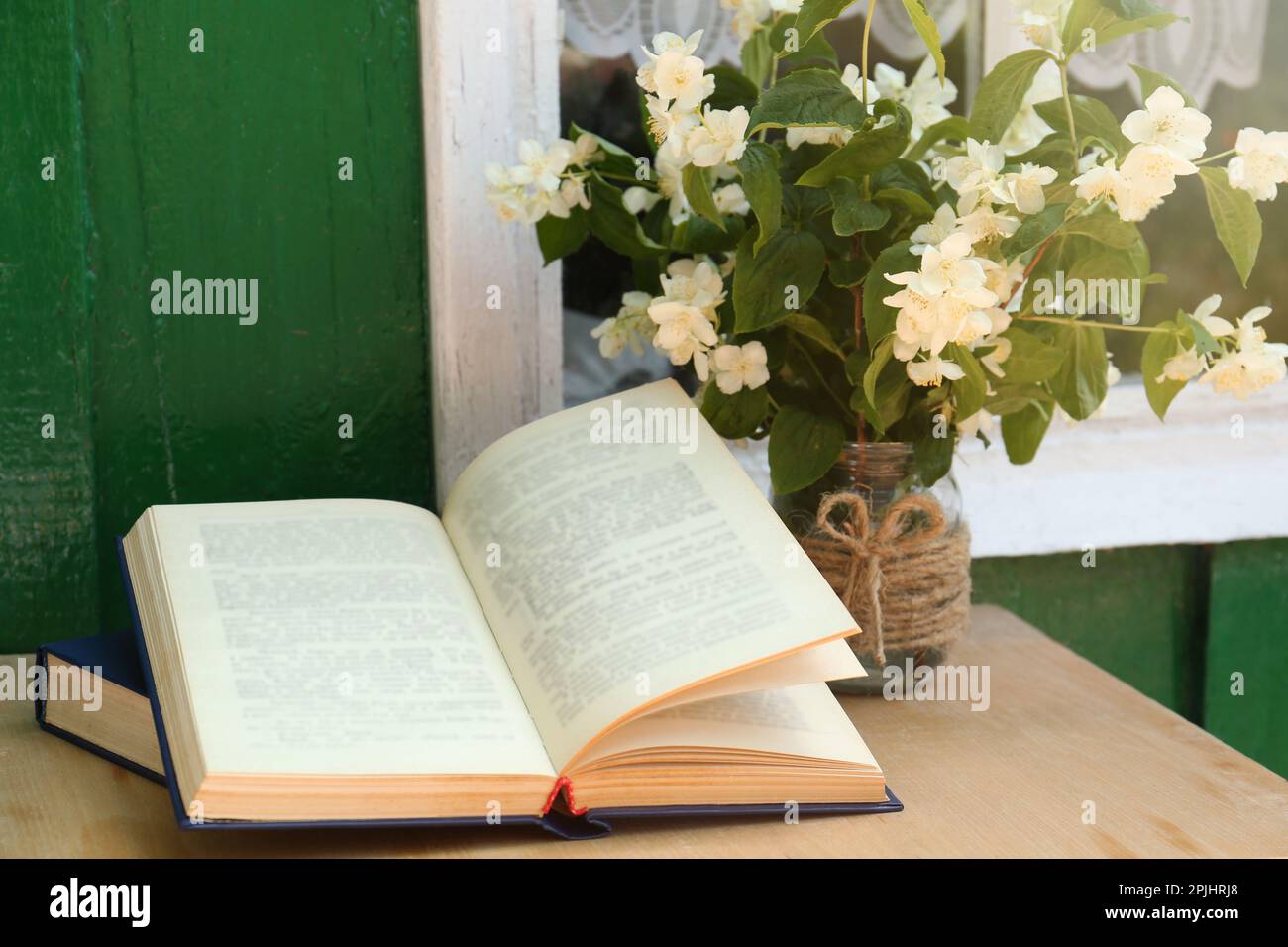 Libri e bellissimi fiori di gelsomino su un tavolo di legno vicino alla finestra all'aperto Foto Stock