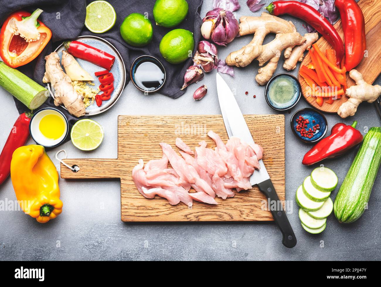 Cibo sfondo. Filetto di pollo a fette e coltello dello chef sul tagliere., verdure, zenzero, lime, peperoncino, aglio, salsa di soia e aceto di riso Foto Stock